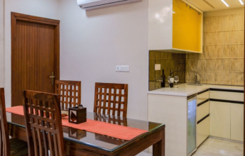 A modern dining area with a wooden table and chairs, adjacent to a compact open kitchen featuring yellow upper cabinets.