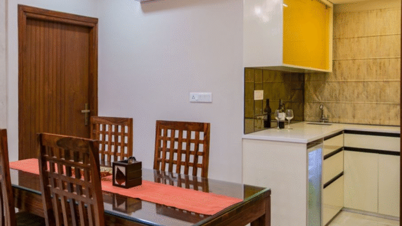 A modern dining area with a wooden table and chairs, adjacent to a compact open kitchen featuring yellow upper cabinets.